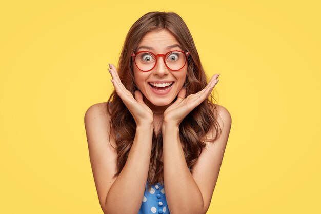 Satisfecho lleno de alegría joven con gafas posando contra la pared amarilla