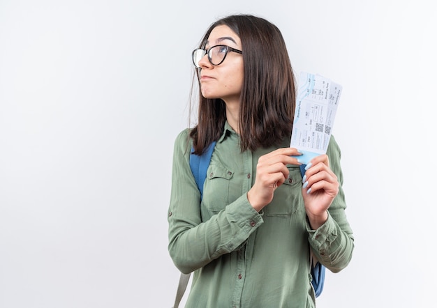 Foto gratuita satisfecho mirando hacia arriba joven escuela mujer con gafas con mochila sosteniendo boletos