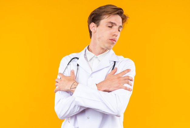 Satisfecho con los ojos cerrados joven médico vistiendo bata médica con estetoscopio aislado en la pared naranja