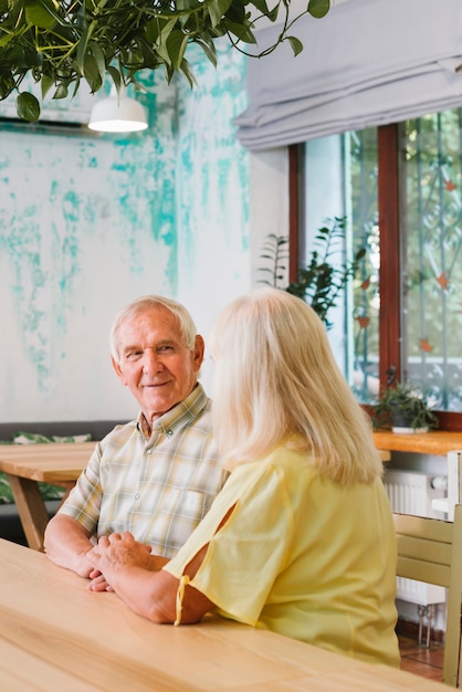 Foto gratuita satisfecho pareja senior sentado en la cafetería y cogidos de la mano