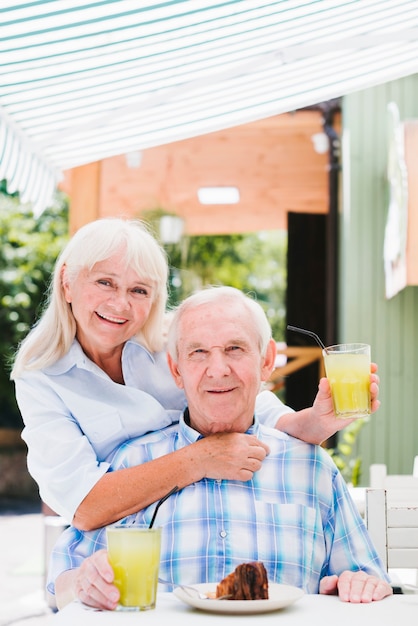 Foto gratuita satisfecho senior pareja abrazándose en la cafetería en la terraza disfrutando de una bebida refrescante y pastel