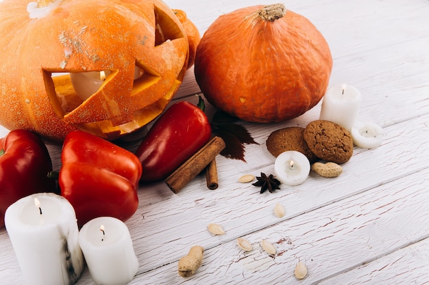 Scarry calabaza de Halloween de pie en la mesa con velas, canela, pimiento rojo y nueces