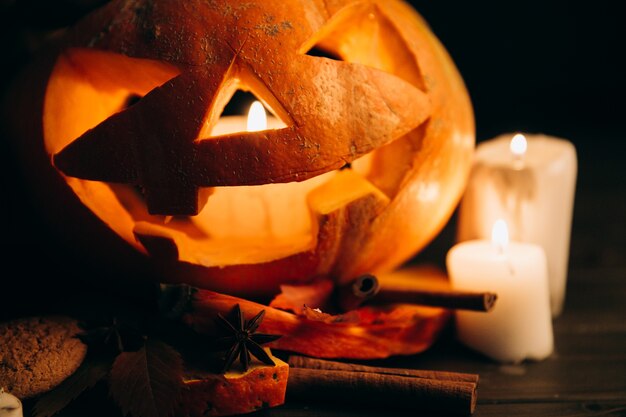 Scarry calabaza de Halloween de pie en la mesa con velas y canela