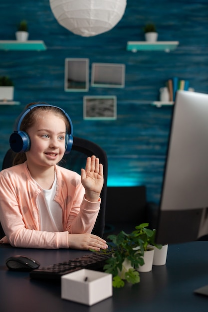 Schoolkid sonriente con auriculares saludando al maestro remoto durante la videollamada en línea