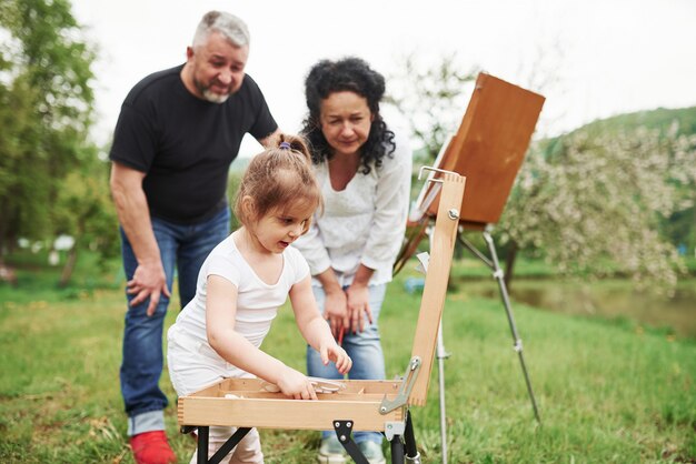 Sé lo que tengo que hacer. La abuela y el abuelo se divierten al aire libre con su nieta. Concepción de la pintura