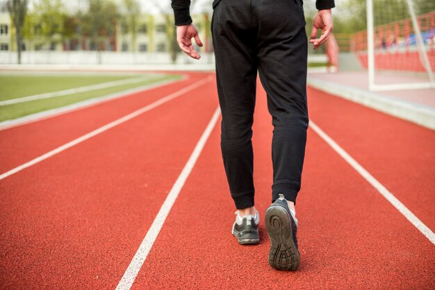 Sección baja de un atleta masculino caminando en pista roja