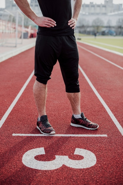 Foto gratuita sección baja de un atleta masculino en la línea de inicio de la pista de carreras con el número tres