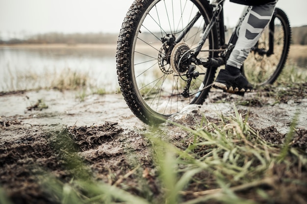 Sección baja del ciclista masculino que monta la bicicleta en fango