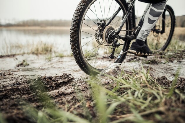 Sección baja del ciclista masculino que monta la bicicleta en fango