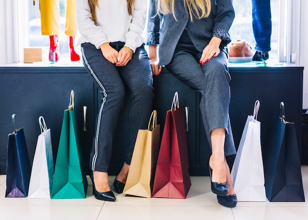 Sección baja de dos mujeres sentadas en la tienda con coloridos bolsos de compras