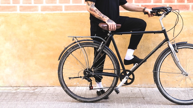 Sección baja de un hombre con bicicleta contra muro pintado y ladrillo.