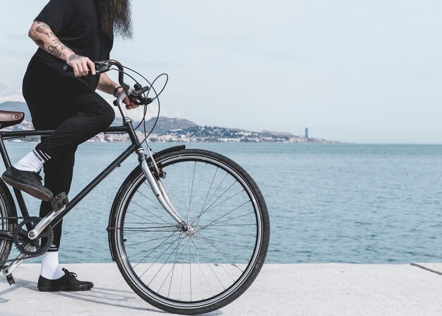 Sección baja de un hombre que monta la bicicleta en la calle cerca del puerto.