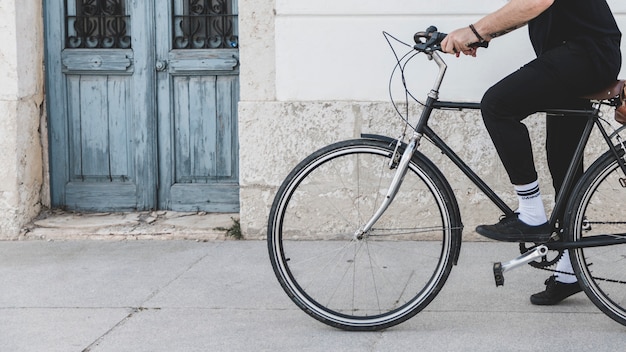 Sección baja de un hombre que monta la bicicleta en la calle.