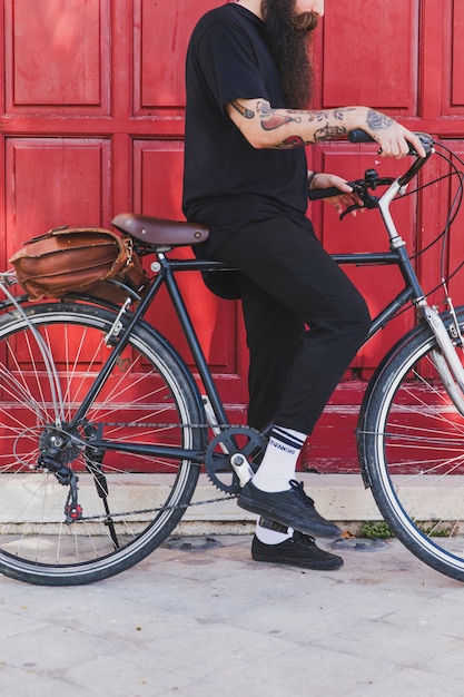 Sección baja de un hombre sentado con bicicleta delante de la puerta.