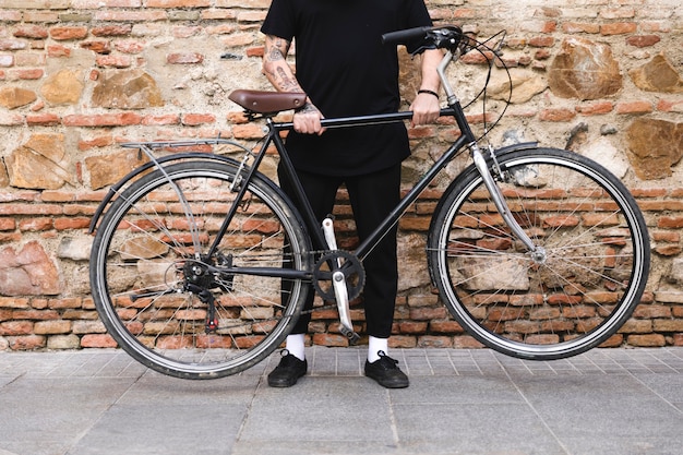 Sección baja de un hombre sosteniendo bicicleta con sus dos manos.