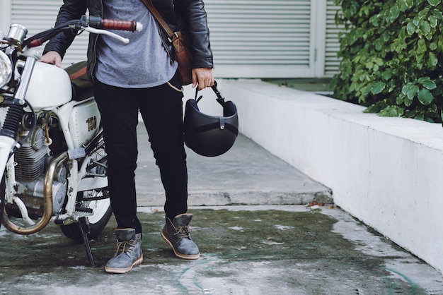 Sección baja de motociclista irreconocible con casco parado en su moto blanca