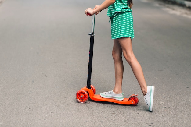 Sección baja de una niña montando scooter en la calle