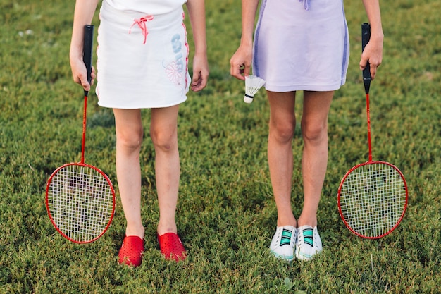 Sección baja de una niña de pie sobre la hierba verde con bádminton y volante