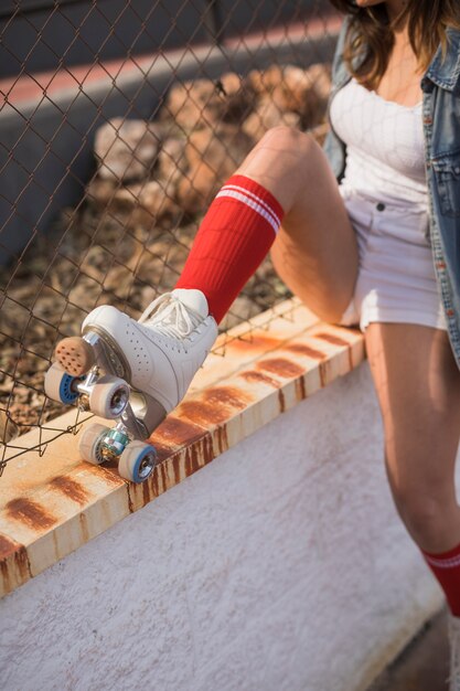 Sección baja de una patinadora sentada cerca de la cerca.