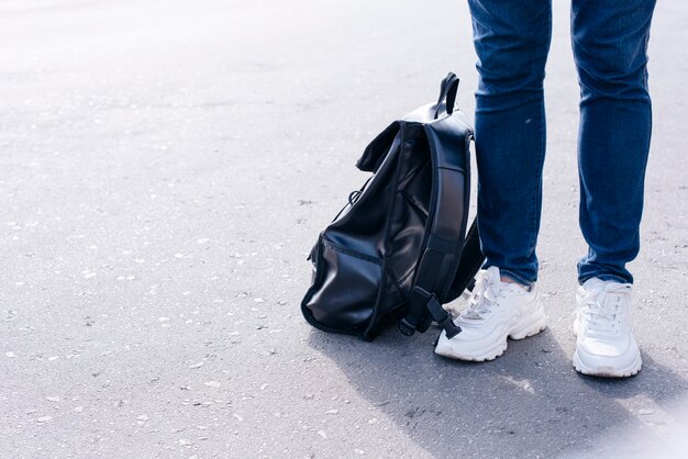 Sección baja de una persona parada en la calle con mochila negra.