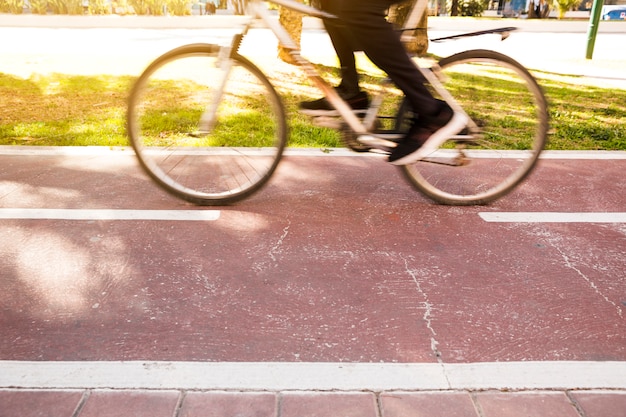 Sección baja de una persona que monta la bicicleta en el parque.