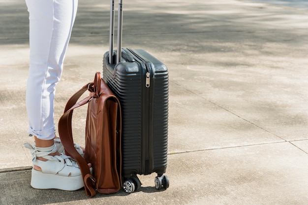 Sección baja de turista femenina de pie en la carretera con equipaje y bolsa de cuero