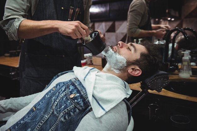 Sección intermedia de barbero aplicando crema en la barba de los clientes