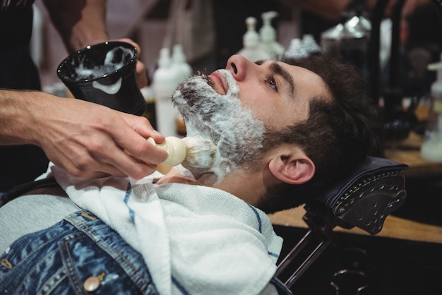 Foto gratuita sección intermedia de barbero aplicando crema en la barba de los clientes