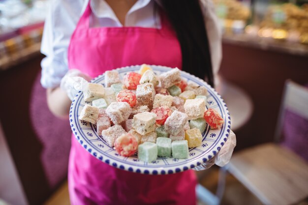 Sección intermedia de mujer comerciante sosteniendo la bandeja de dulces turcos en el mostrador