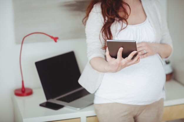 Sección intermedia de mujer embarazada con tableta digital en la sala de estudio