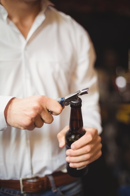 Sección media del barman abriendo una botella de cerveza