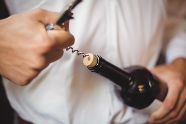 Foto gratuita sección media del barman abriendo una botella de vino