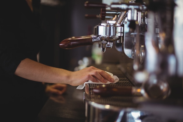 Foto gratuita sección media de la camarera limpiando la máquina de café espresso con una servilleta en el café