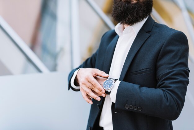 Sección media del empresario sosteniendo el reloj de pulsera en su mano