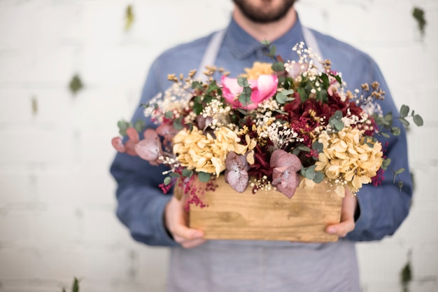 Sección media del hombre que sostiene el cajón de madera con flores de colores