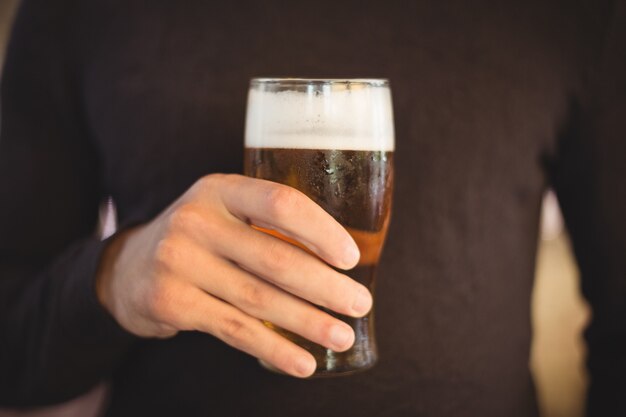 Sección media del hombre que sostiene un vaso de cerveza