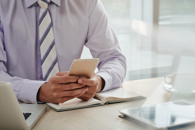 Sección media del hombre revisando correos electrónicos en el teléfono inteligente