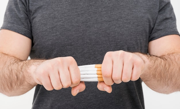 Sección media de un hombre rompiendo el paquete de cigarrillos con las dos manos