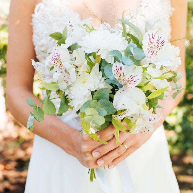 Sección media de las manos de una novia con un hermoso ramo de flores