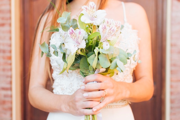 Sección media de las manos de una novia con un hermoso ramo de flores