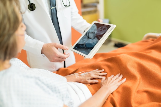 Sección media del médico que muestra el informe de rayos X en la tableta digital al paciente mayor en el hospital