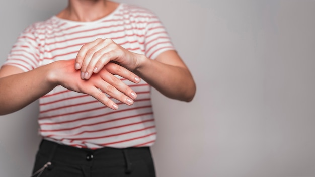 Sección media de la mujer joven que tiene dolor en la mano contra fondo gris