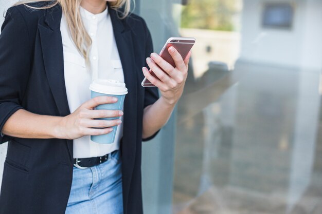 Sección media de la mujer que sostiene la taza de café de la disposición que sostiene smartphone