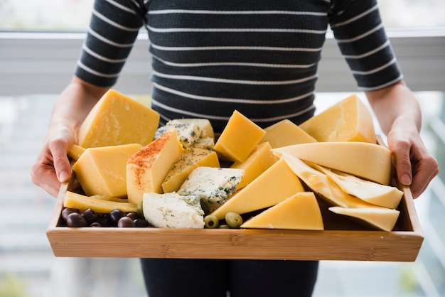 Foto gratuita sección media de mujer con rebanadas de queso en bandeja de madera