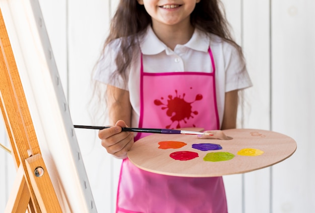 Foto gratuita sección media de una niña sonriente con pincel y paleta