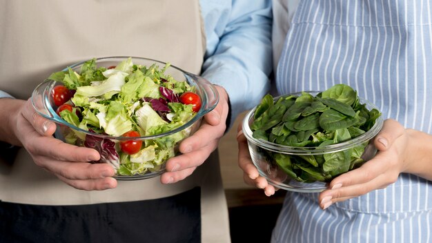 Sección media de pareja sosteniendo un tazón de ensalada saludable y hojas de albahaca