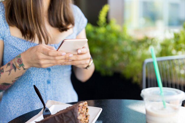 Sección media de personas influyentes que comparten historias de comida en línea a través de un teléfono inteligente en el café