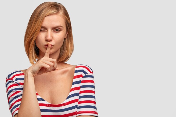 Foto gratuito secreta joven delgada con mirada seria y misteriosa, parpadea y muestra el signo de silencio, tiene el pelo corto claro