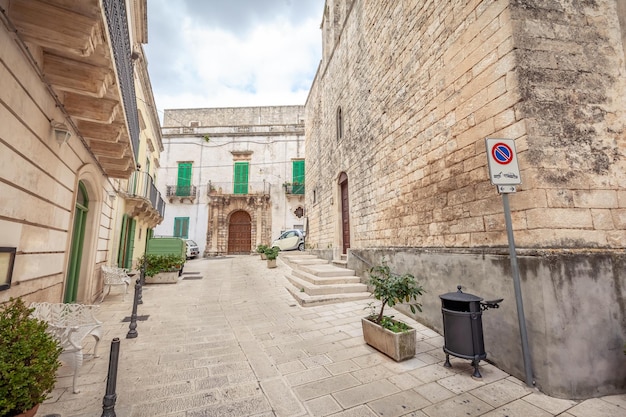 Seductora vista de las calles vacías del casco antiguo de Martina Franca con bonitas casas pintadas de blanco entre la vegetación. Maravilloso día en una ciudad turística, Apulia, Italia.