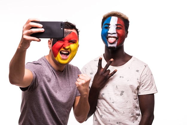 Los seguidores de los aficionados al fútbol con la cara pintada de los equipos nacionales de Francia y Alemania toman selfie aislado sobre fondo blanco.